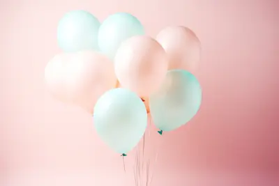 Une grappe de ballons de baudruche pastel, roses et vert d'eau, sur un mur rose pâle