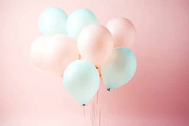 Une grappe de ballons de baudruche pastel, roses et vert d'eau, sur un mur rose pâle