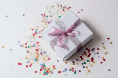 Un paquet cadeau blanc noué d'un ruban rose, entouré de confettis de couleur sur une table blanche