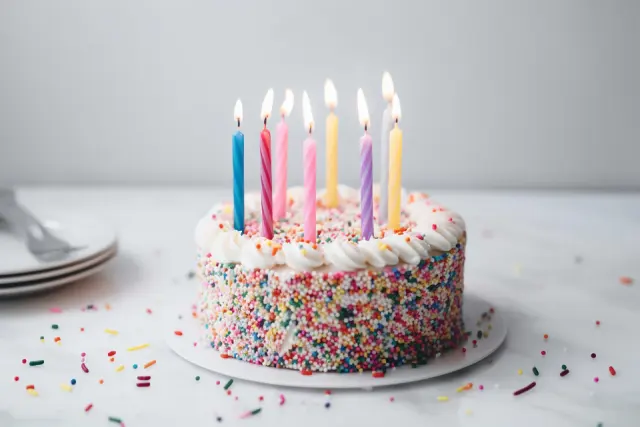 Gâteau d'anniversaire couvert de vermicelles de couleur, avec des bougies allumées