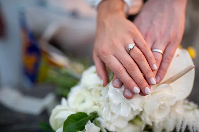Deux mains portant des alliances posées l'une sur l'autre au-dessus d'un bouquet de fleurs blanches
