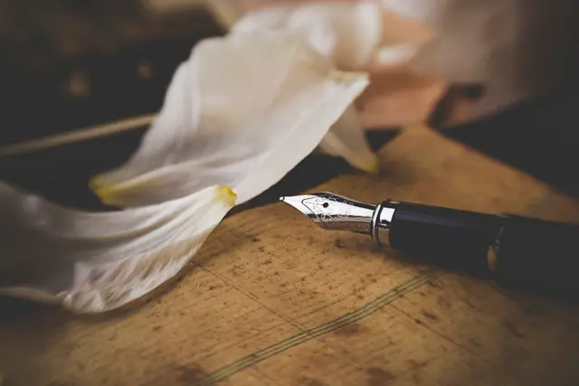 Un stylo-plume à la plume argentée posé sur une vieille feuille manuscrite, à côté d'une fleur blanche